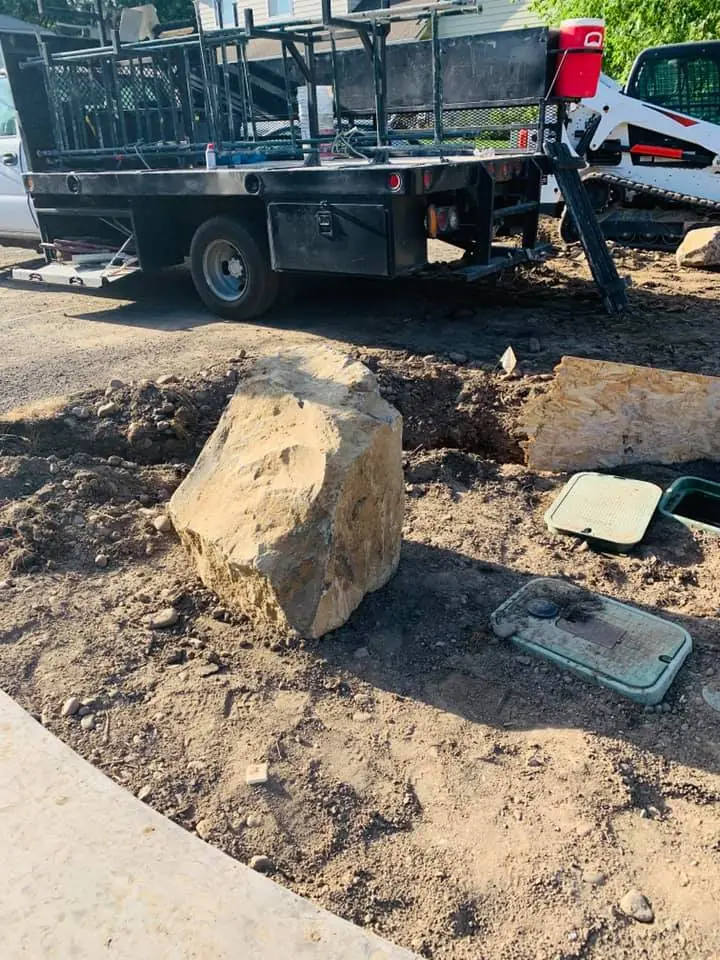 Work truck and loader on site with a large landscape boulder set in place
