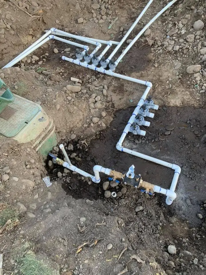 Rebuilt sprinkler valve manifold with new white PVC lines in an open trench